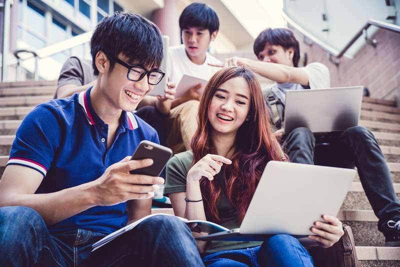 asian-students-discussing-something-holding-smartphone-laptop